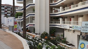 Un hotel de varios pisos con un llamativo letrero 'TAMAR', mesas al aire libre y un cartel de alquiler de coches.
