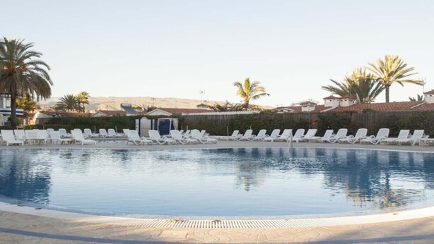 Una piscina con sillones blancos y palmeras al fondo.