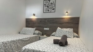 Habitación de hotel con dos camas, cada una con ropa de cama y almohadas estampadas con motivos florales. Hay luces fijadas a la pared y una obra de arte enmarcada sobre las camas.
