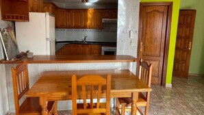 A kitchen with wooden cabinets, a white refrigerator, a dining table with chairs, and a green accent wall. - An oasis with a double panoramic view over the ocean and the mountain El Teide 2 (Icod de los Vinos)