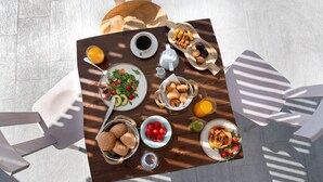 Una mesa de desayuno con diversos alimentos y bebidas, rodeada de sillas blancas.