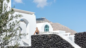 Un edificio blanco con pared de piedra, ventana azul y una montaña al fondo.