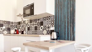 A modern kitchen with a patterned backsplash, a microwave, and a kettle on the counter. There are two white chairs around a wooden table. - Your modern retreat in the heart of Rochefort - A unique experience (Rochefort)