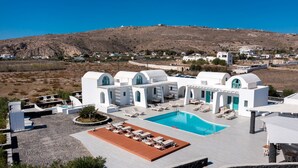 A resort with a swimming pool, sun loungers, and a view of a hilly landscape. - Santa Irina Luxury Sunny Lofts 4 (ΣΑΝΤΟΡΙΝΗ)