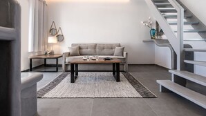 A modern living room with a sofa, coffee table, and a staircase. - Santa Irina Luxury Sunny Lofts 4 (ΣΑΝΤΟΡΙΝΗ)
