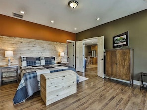 A bedroom with a wooden headboard, a bed with a plaid bedspread, a nightstand with a lamp, a wardrobe, and a television on the wall.