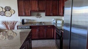 A kitchen with dark wooden cabinets, a stainless steel refrigerator, and a granite countertop.