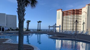 A pool area with lounge chairs, palm trees, and a building with balconies.
