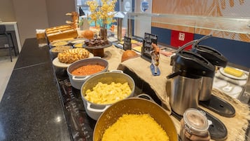 A buffet with various food items, a coffee machine, and a decorative vase with yellow flowers.