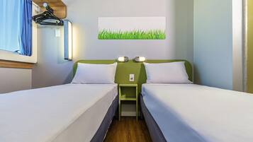 A hotel room with two beds, a nightstand, a wall-mounted lamp, and a window with curtains.
