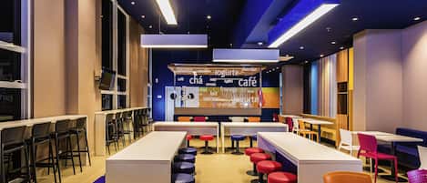 A modern café interior with a central counter displaying menu items, multiple seating arrangements including bar stools and tables, and a contemporary ceiling design with recessed lighting.