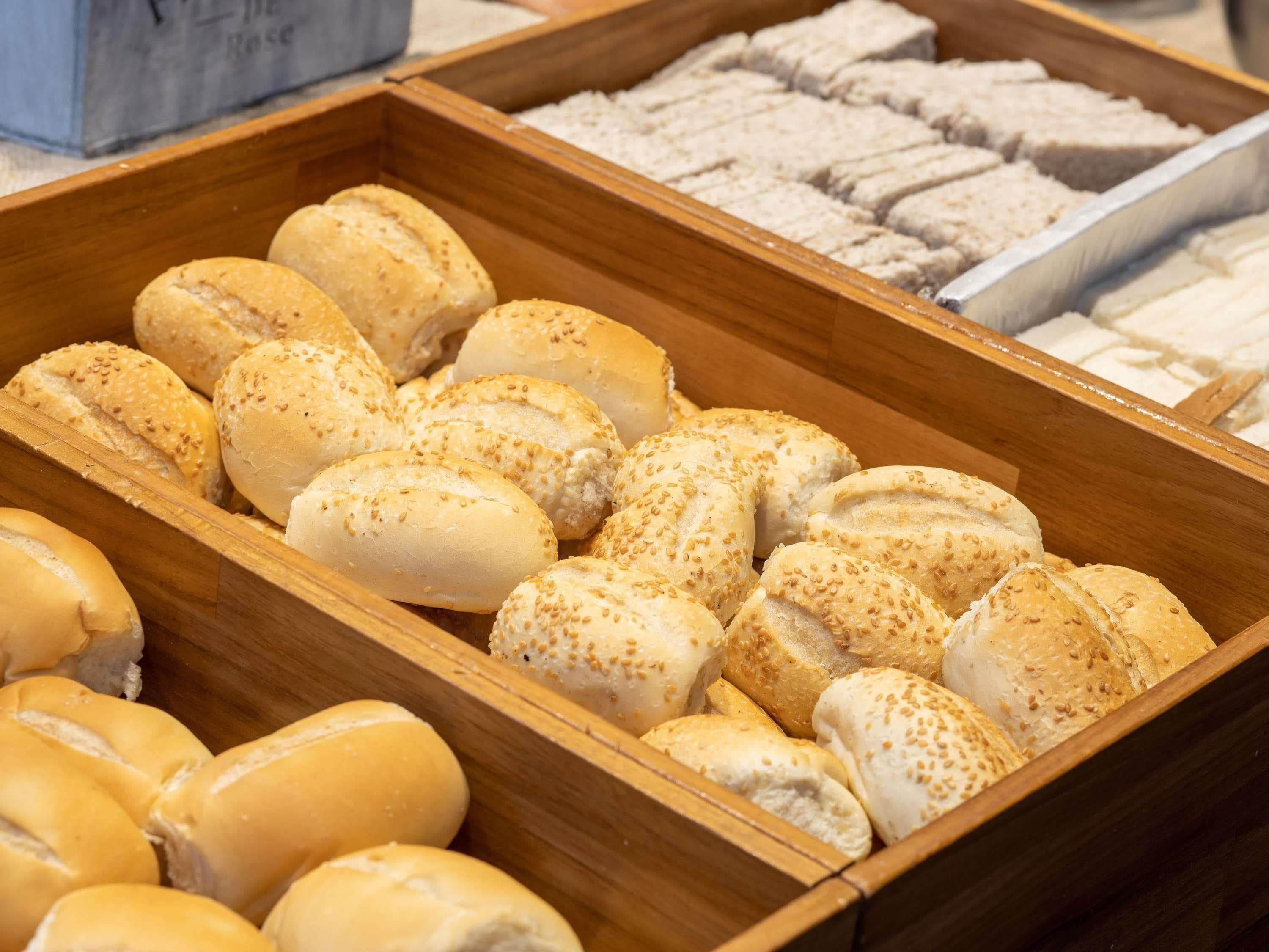 Una exhibición de pan de madera con bollos de sésamo y otras variedades.