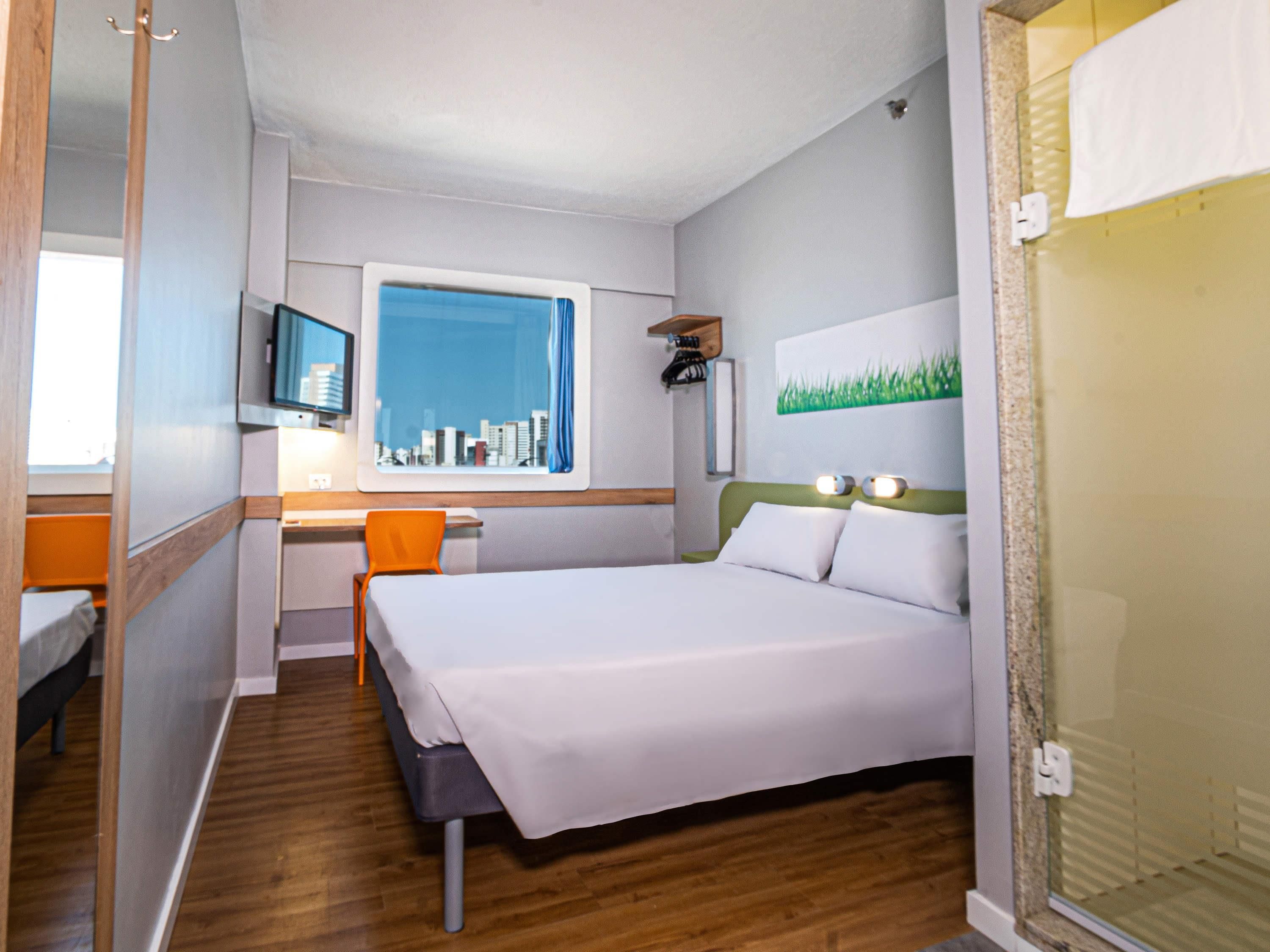 Hotelkamer met een bed, bureau, stoel, televisie en raam met uitzicht op de stad.