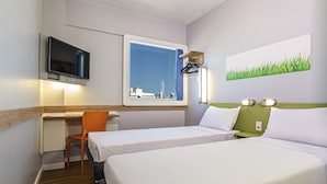 Habitación de hotel con dos camas, un escritorio, una silla, un televisor, una ventana con vista a la ciudad y un cuadro de césped.