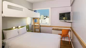 Quarto de hotel com uma cama beliche, uma mesa com cadeira, uma televisão e uma janela com vista para a cidade.