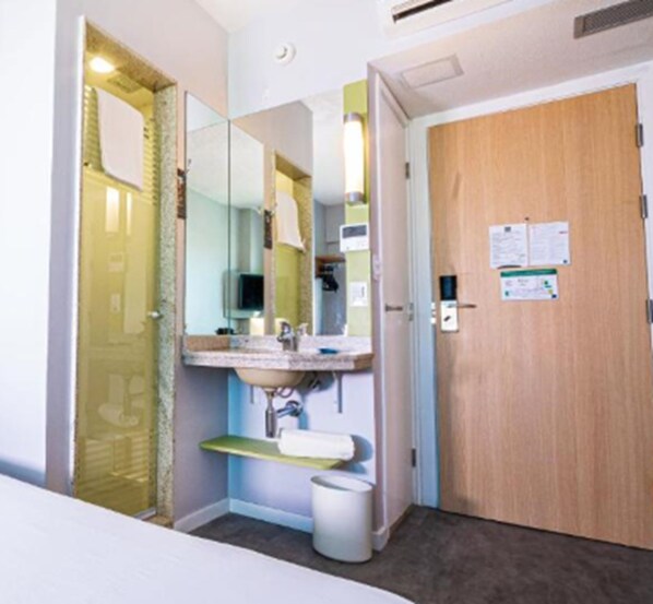 A small bathroom with a sink, mirror, and a wooden door. - ibis Budget Fortaleza Praia De Iracema (Fortaleza)