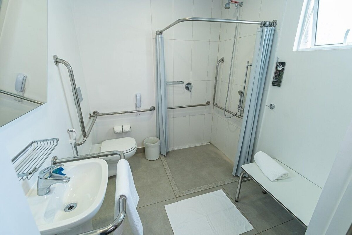 A modern bathroom with a shower, toilet, sink, and a bench.