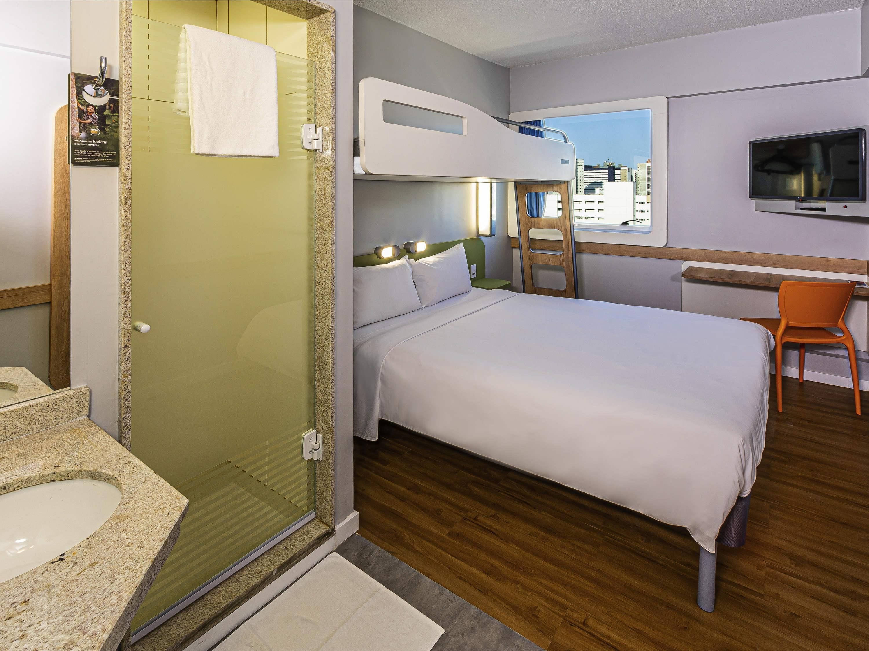 Camera d'albergo con un letto, una scrivania con una sedia, una televisione e un box doccia.