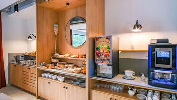 Una kitchenette moderna con armarios de madera, una cafetera, un dispensador de jugo y un refrigerador pequeño.