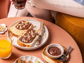 Une table de petit-déjeuner avec des tartines garnies de chocolat et de noix, un bol de pâte à tartiner au chocolat et un verre de jus d’orange.