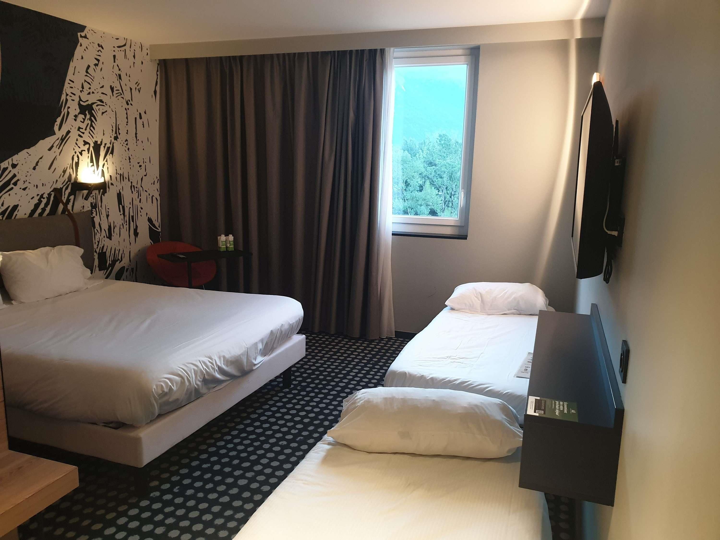 Een hotelkamer met twee bedden, een raam met gordijnen, een flatscreen televisie en een klein tafeltje.