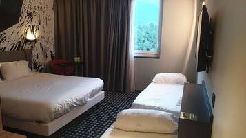 Een hotelkamer met twee bedden, een raam met gordijnen, een flatscreen televisie en een klein tafeltje.