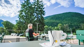 A table with a cup and saucer, a person in the background, and a mountain view.