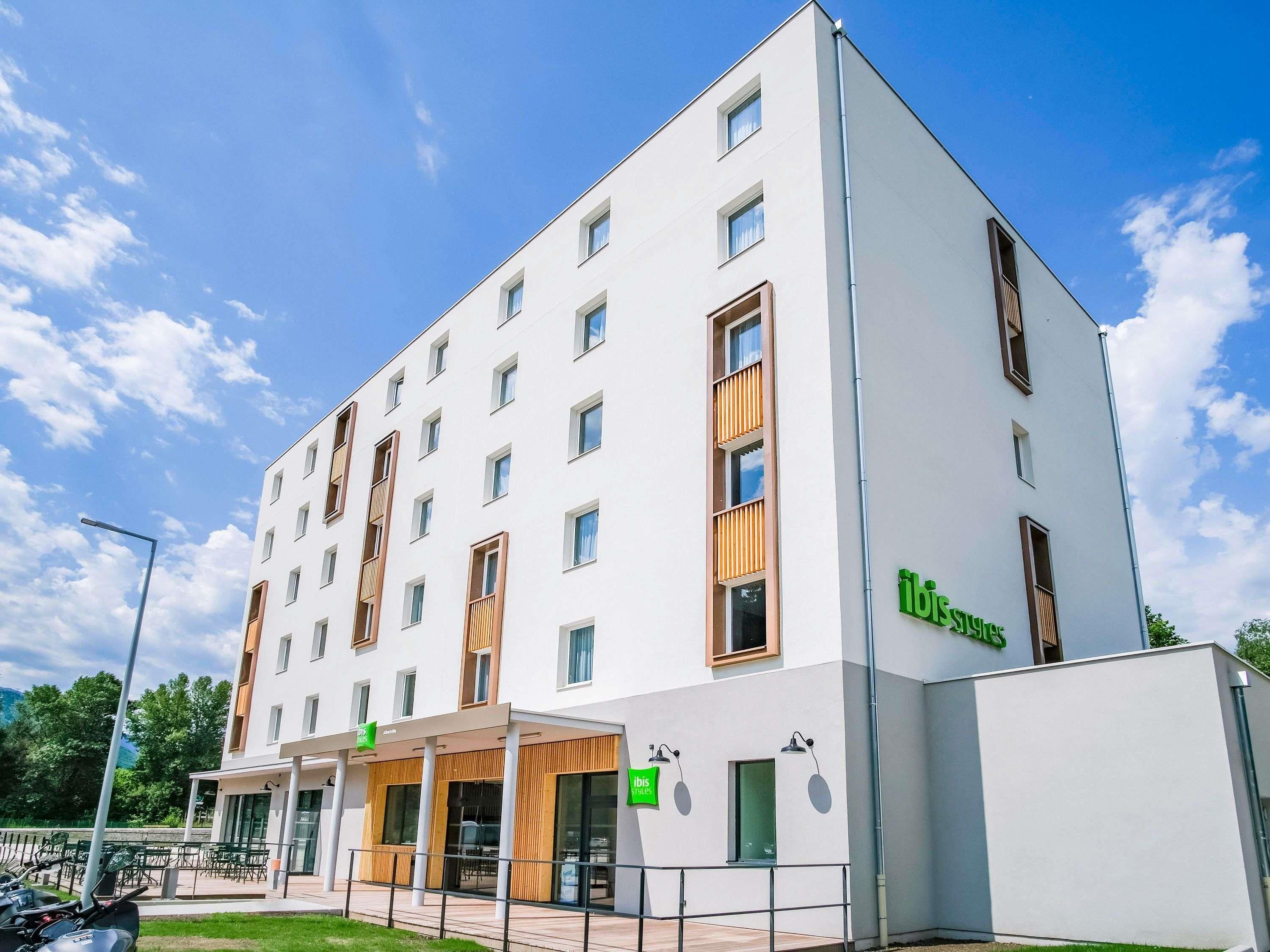 Un hôtel moderne à la façade blanche, doté de nombreuses fenêtres et d’une enseigne verte « ibis styles ».
