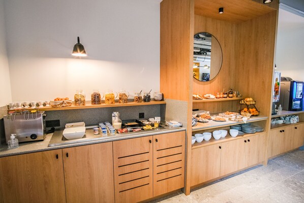 Ein Frühstücksbuffet mit verschiedenen Speisen und Getränken, Holzschränken und einem Spiegel an der Wand.