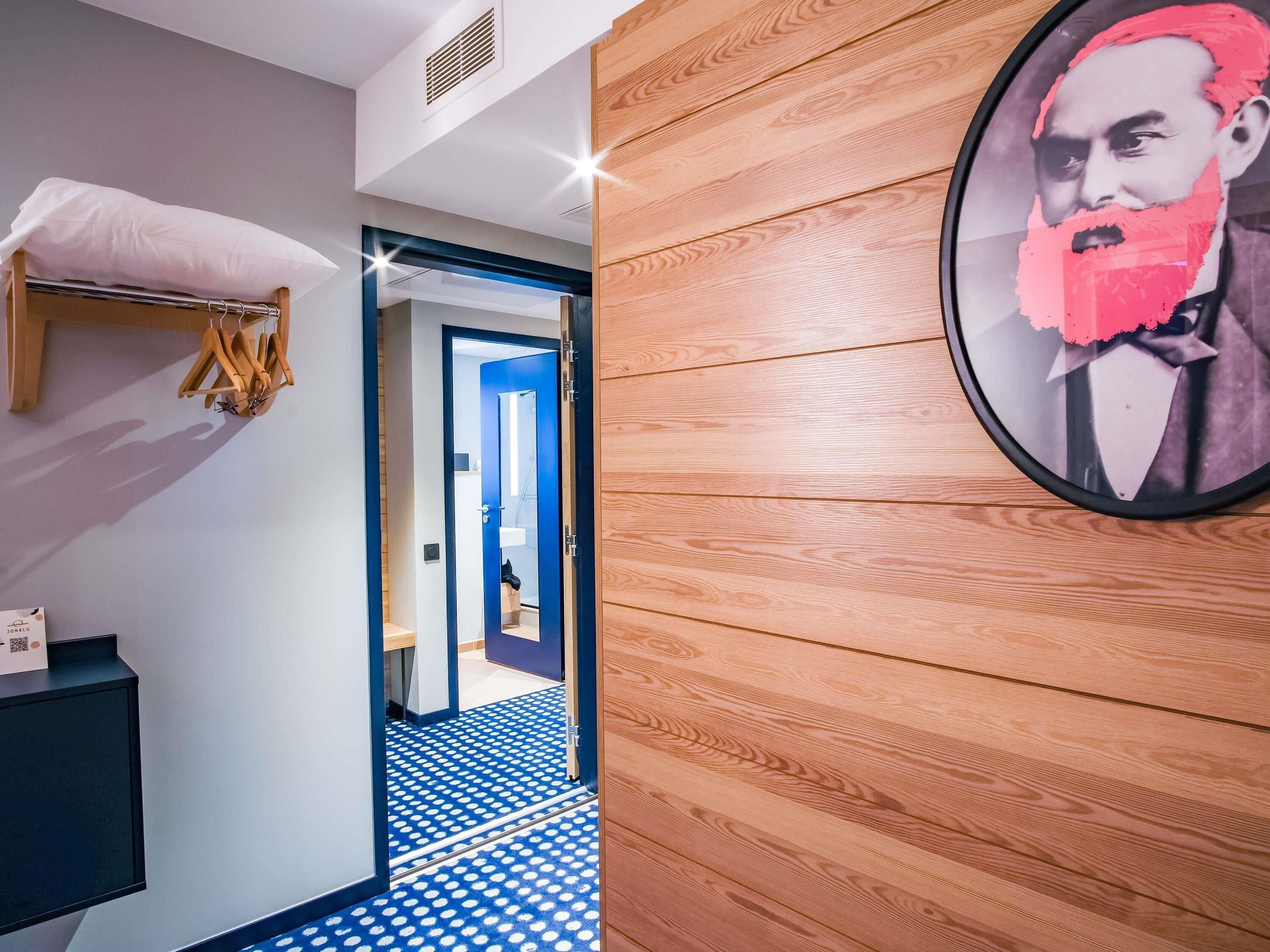 Un pasillo con piso de diseño azul y blanco, una pared de madera con un cuadro enmarcado y una puerta que da a otra habitación.