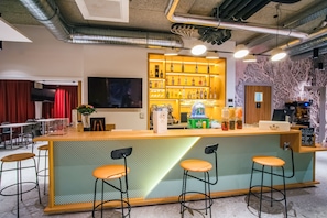 Un espace bar avec un comptoir, des tabourets, un téléviseur et une étagère remplie de bouteilles.