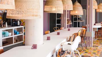 A modern dining area with white tables, wicker pendant lights, and colorful patterned flooring.