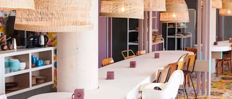 A modern dining area with white tables, wicker pendant lights, and colorful patterned flooring.