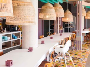 A modern dining area with white tables, wicker pendant lights, and colorful patterned flooring.
