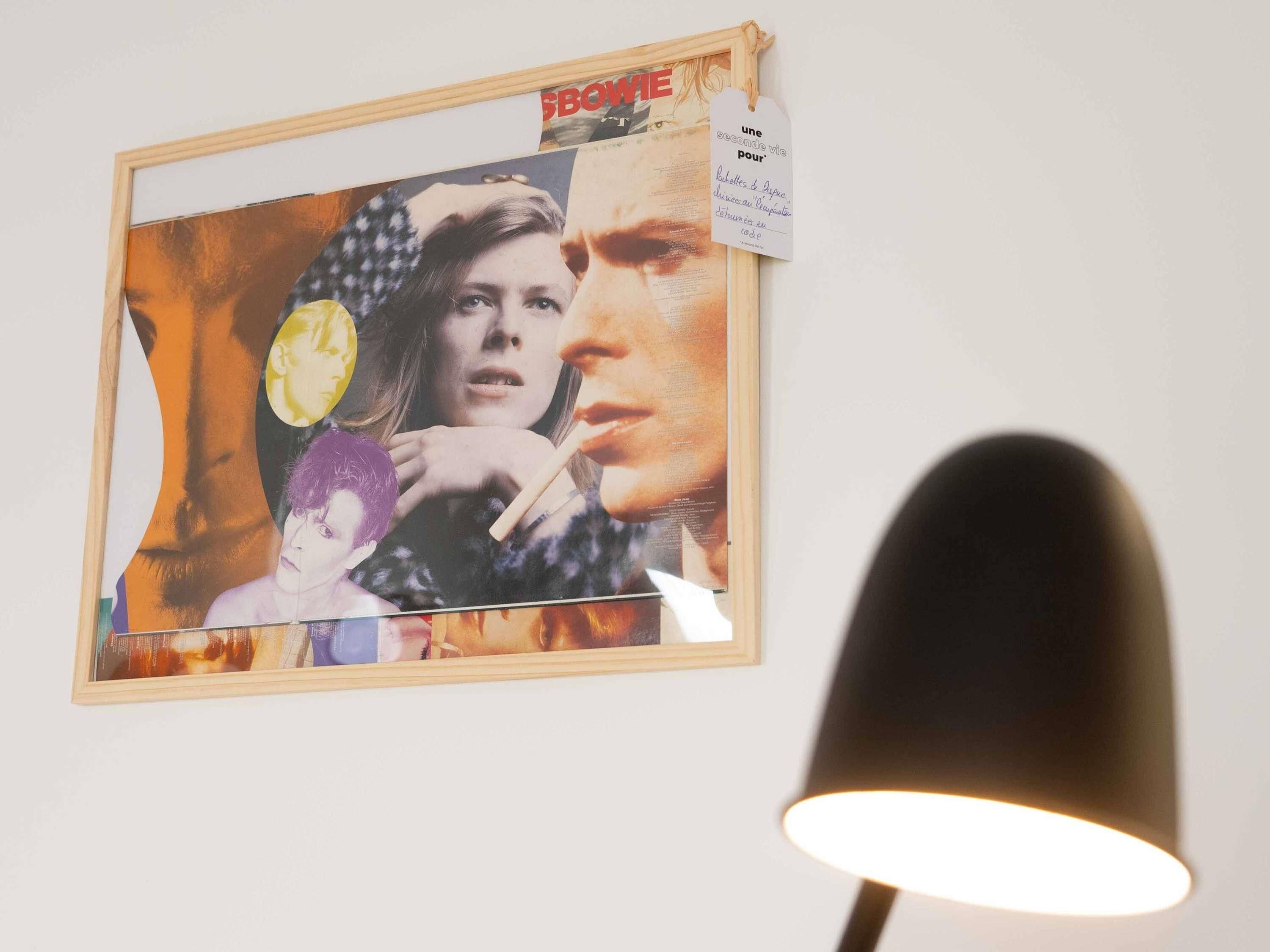 Una obra enmarcada con un collage de imágenes en una pared, una lámpara y una etiqueta con texto.