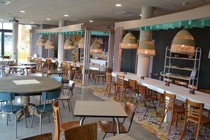 Un restaurante con mesas y sillas redondas, lámparas colgantes y un patrón de piso colorido.