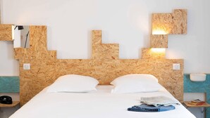 A hotel room with a wooden headboard, two white pillows, a neatly made bed, a bedside table with a lamp, and a small shelf with books. - Greet Hotel Rennes Pace (Pace)