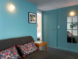A room with teal walls, a grey sofa with patterned cushions, a small table with a tray, and a framed picture on the wall. - Greet Hotel Rennes Pace (Pace)
