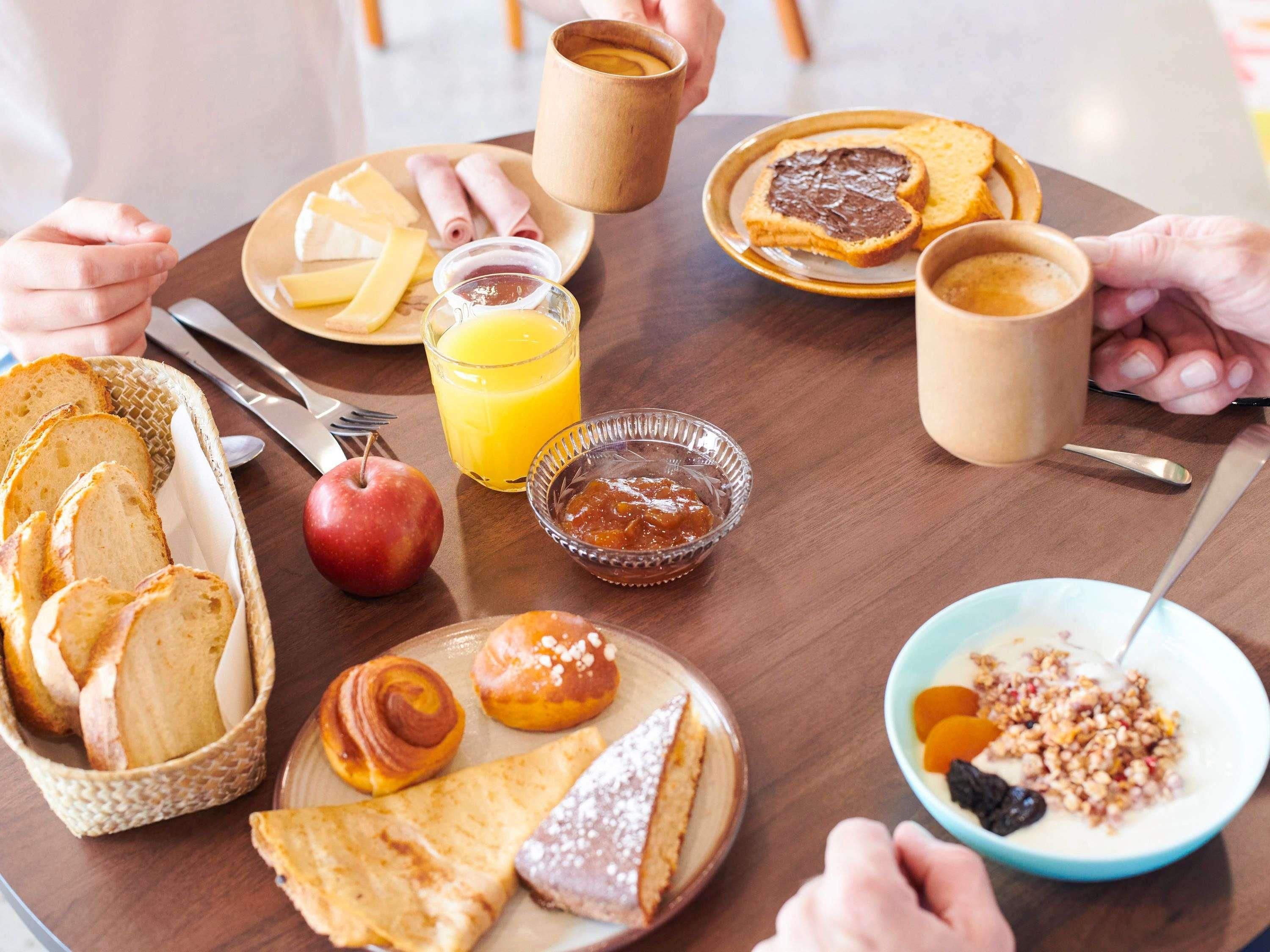 Une table en bois dressée pour le petit-déjeuner, avec du pain, des viennoiseries, des fruits et des boissons.