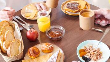 Une table en bois dressée pour le petit-déjeuner, avec du pain, des viennoiseries, des fruits et des boissons.