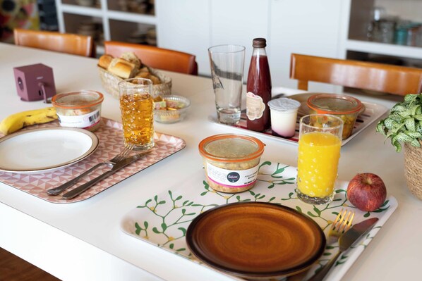 Una mesa de desayuno servida con platos, cubiertos, un vaso de zumo de naranja, una botella de agua, un tarro de mermelada y un plátano.