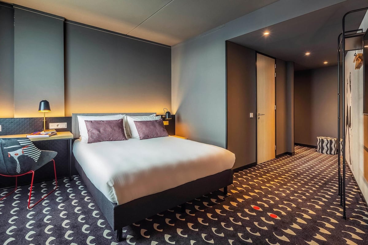 Una habitación de hotel moderna con cama, mesita de noche, lámpara y alfombra estampada.