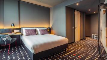A modern hotel room with a bed, bedside table, lamp, and a patterned carpet.