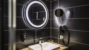 Un baño moderno con un lavamanos blanco, un espejo redondo con una luz tenue alrededor y un espejo de mano.