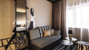 A modern hotel room with a sofa, a small round table, a mirror, and a large window with curtains. - ibis Styles Arnhem Centre (Arnhem)
