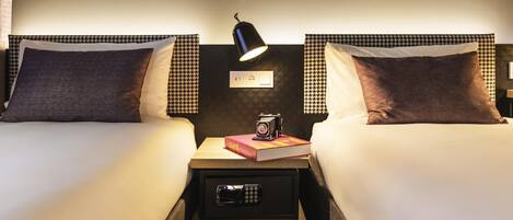 A hotel room with two beds, a nightstand with a lamp, a camera, and a book.