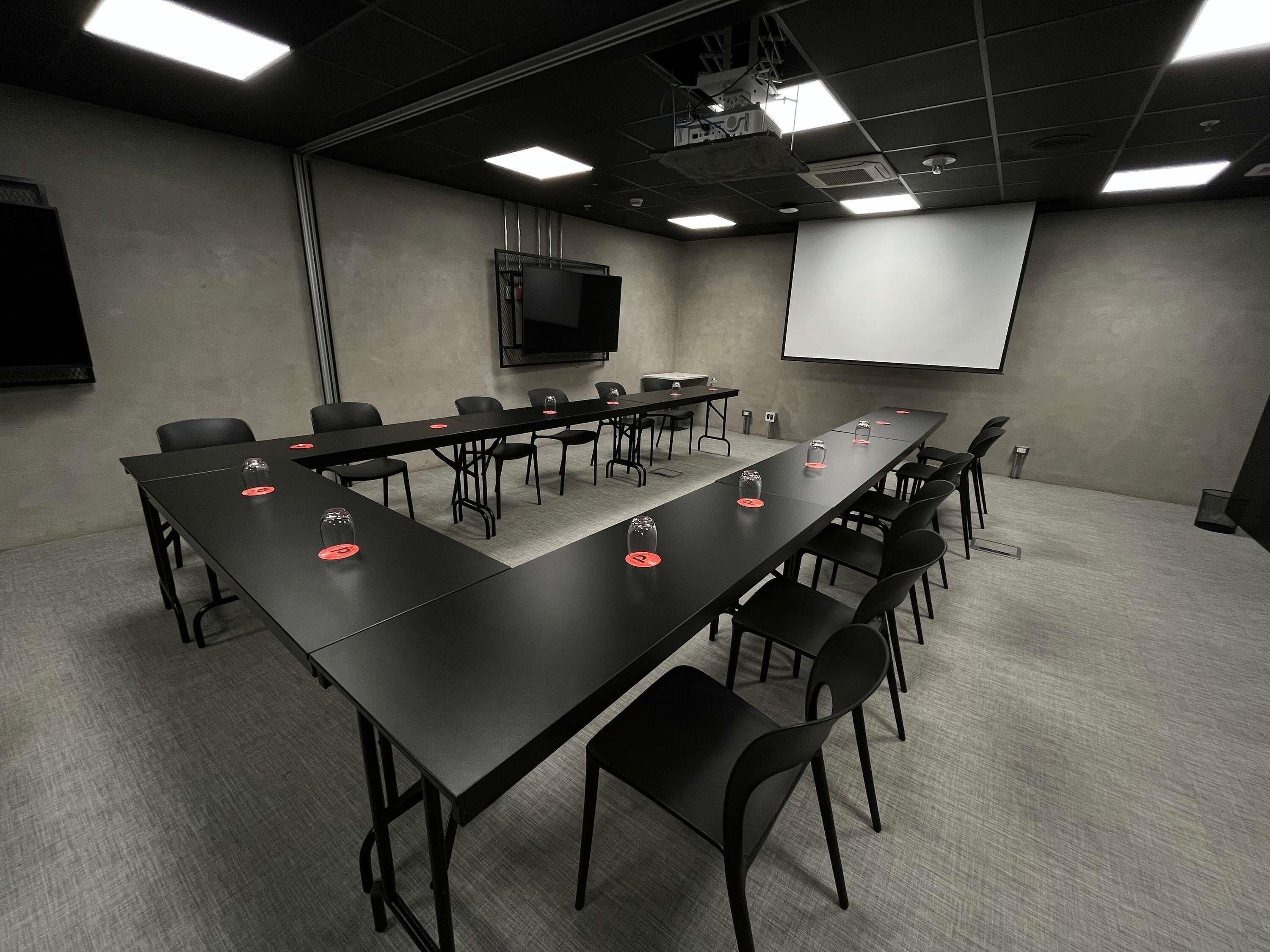 Un salón de conferencias con una larga mesa, sillas, una pantalla de proyector y una televisión.