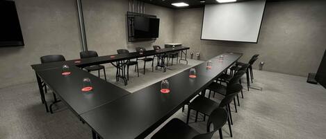 A conference room with a long table, chairs, a projector screen, and a television.