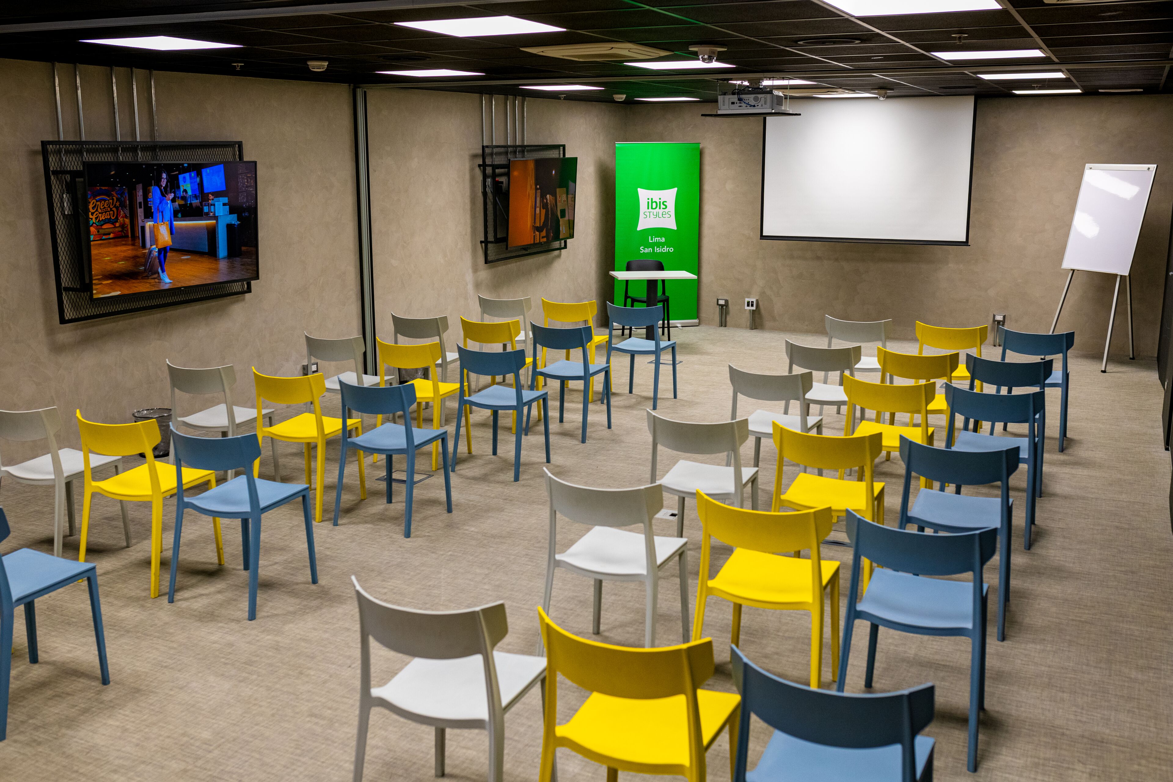 A conference room with rows of chairs, a large screen, and a projection screen.
