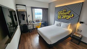 A hotel room with a bed, a desk with a laptop, a coffee maker, and a mirror.